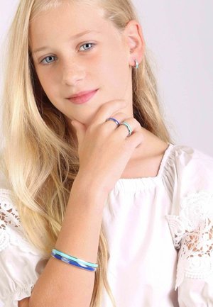 Zilveren en kleurrijke ringen aan vingers, blauwe en turkooise armband om pols, meisje met lang haar dat een witte blouse met kantaccenten draagt.