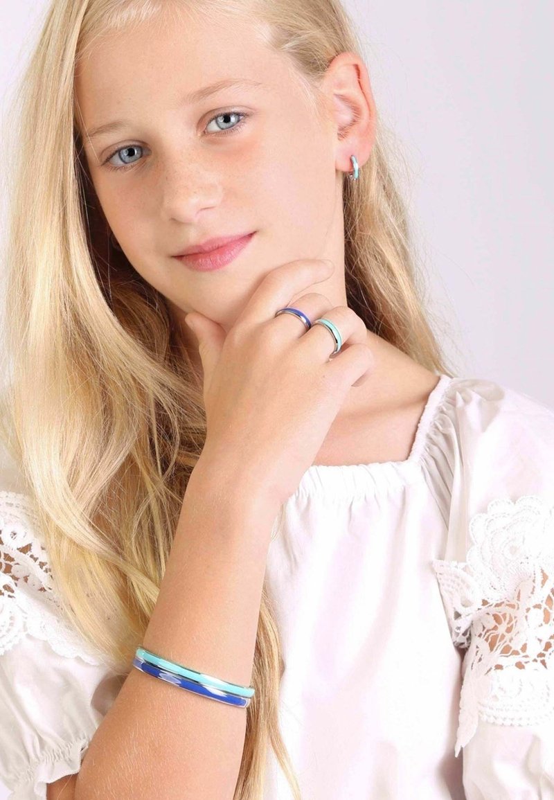 Zilveren en kleurrijke ringen aan vingers, blauwe en turkooise armband om pols, meisje met lang haar dat een witte blouse met kantaccenten draagt.