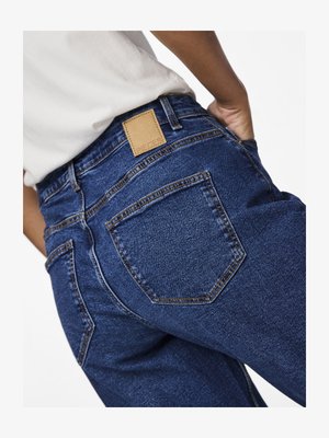 Modré rifle s vysokým pásom, vyrobené z hladkej denimovej tkaniny, s zadnými vreckami a koženým štítkom značky na páse.