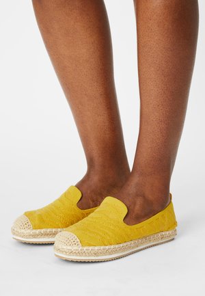 Yellow slip-on shoes with a textured fabric upper, woven jute trim, and a rounded canvas toe cap. The sole is flat and beige.