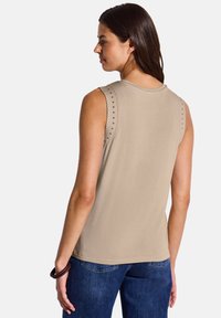 Top beige senza maniche con accenti di borchie sulle spalle, realizzato in tessuto morbido, con scollatura rotonda e vestibilità rilassata.
