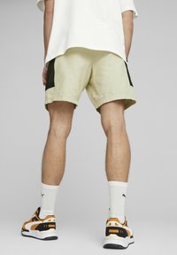 Shorts beige con pannelli laterali neri, vestibilità rilassata, abbinati a sneakers arancioni e nere, e calze bianche a crew visibili sopra la caviglia.