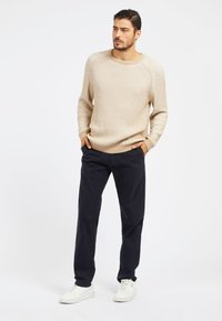 Maglione in maglia a coste beige con maniche lunghe, collo a giro, abbinato a pantaloni blu navy e sneakers bianche. Tessuto liscio, vestibilità morbida.