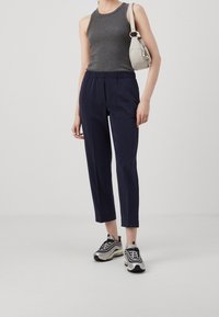 Tummansinisiä, kapenevia housuja elastisella vyötäröllä, yhdistettynä harmaaseen hihattomaan puseroon ja mustiin sekä hopeisiin lenkkareihin. Kevyt käsilaukku viimeistelee asun.