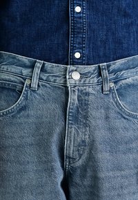 Vaqueros de mezclilla azul claro con un diseño clásico de cinco bolsillos, que cuentan con un cierre de botón de metal y sutiles detalles de desgaste.