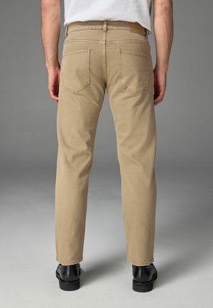 Pantalon en coton beige avec une coupe droite, doté de deux poches arrière et d'un patch en cuir au-dessus de la taille.