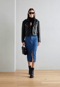 Giacca di pelle nera, dolcevita nero, gonna a matita in denim blu con spacco frontale, stivali da combattimento neri e una piccola borsa nera. Occhiali da sole indossati.