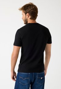 Czarny bawełniany T-shirt z krótkimi rękawami, okrągłym dekoltem i gładką fakturą, w zestawieniu z niebieskimi dżinsami z detalami stębnowania w tylnej kieszeni.