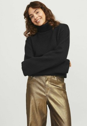 Maglione nero a collo alto in maglia con maniche lunghe, abbinato a pantaloni metallici dorati. Il maglione presenta una vestibilità rilassata e un tessuto testurizzato.