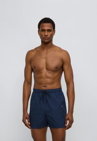 Μπλε ναυτικό μαγιό βερμούδα με υφή, ελαστική μέση, ρυθμιζόμενο κορδόνι και λογότυπο στο πλάι.