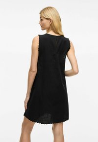 Robe noire aucut décontracté, avec des bords festonnés aux manches et à l'ourlet, et un détail en ouverture dans le dos, fabriquée en tissu léger texturé.