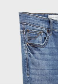 Närbild av blå denimjeans som visar framfickan, myntfickan med nitar, bältesögla och synlig sömnadsdetalj.