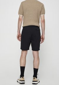 Shorts noirs en tissu doux, dotés d'une taille élastique et d'une poche arrière. Assortis avec un t-shirt en tricot beige et des chaussures de sport.