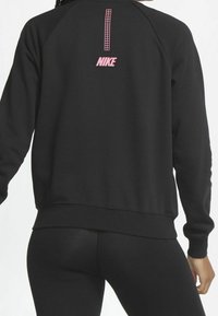 Svart sweatshirt med rosa Nike-logotyp på ryggen, med ett vertikalt designelement. Tillverkad av ett mjukt, texturerat material med raglanärmar.