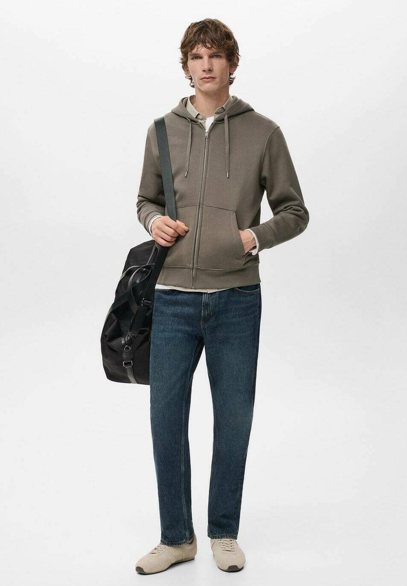 Hooded sweatshirt in muted olive, zippered front, two pockets. Paired with blue jeans and beige sneakers. Black bag with shoulder strap.