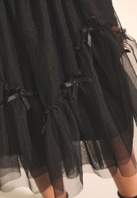 Gonna in tulle nero con più sezioni arricciate e piccoli fiocchi neri. La trama trasparente offre un effetto a strati con un design fluido.