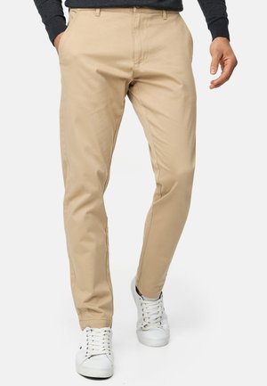 Chinos beige con un corte ajustado, que cuentan con bolsillos laterales y una textura suave. Combinados con zapatillas blancas para un look casual.