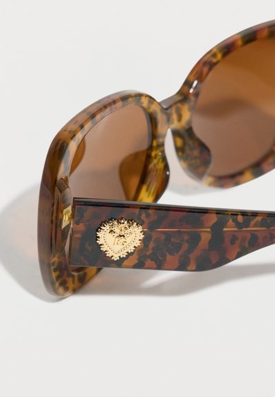 Γυαλιά ηλίου με σχέδιο χελώνας, καφετί φακούς και χρυσό έμβλημα σε σχήμα καρδιάς στο πλάι του βραχίονα.