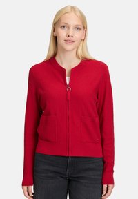 Czerwona kardigan zapinany na zamek, wykonany z teksturowanego materiału dzianinowego, z okrągłym dekoltem, dwiema przednimi kieszeniami i ściągaczami przy rękawach.