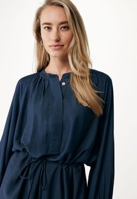 Abito blu navy realizzato in tessuto morbido, con scollatura a bottoni, maniche lunghe e vita regolabile con lacci per una vestibilità comoda.