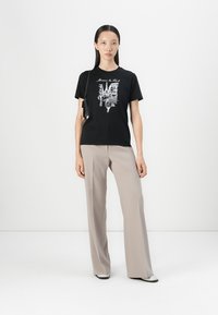 Black cotton t-shirt with a graphic print, paired with beige wide-leg pants, and black-and-white shoes; simple design and relaxed fit.
