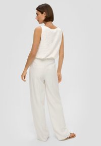 Biała bezrękawnik z kwiatowym haftem w połączeniu z wysokim stanem, szerokimi białymi spodniami. Gładki materiał i luźny krój.