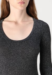 Svart ribbestrikket topp med scoop-utsnitt og lange ermer. Stoffet har en glitrende tekstur med subtile vertikale striper.