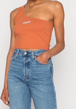 Femme portant un crop top asymétrique orange avec le logo "Levi's" et un jean denim bleu taille haute, une main dans la poche.