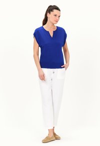 Top azul de manga corta con escote en V y dobladillo acanalado, combinado con pantalones de lino blancos que tienen un bolsillo frontal y zapatos suaves de color marrón claro.