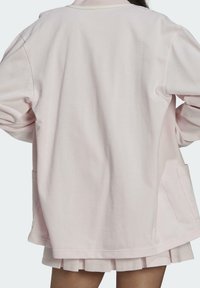 Ljust rosa oversized jacka med en slät textur, med mandarin-krage, sidofickor och långa ärmar. Enkel design med minimal detalj.