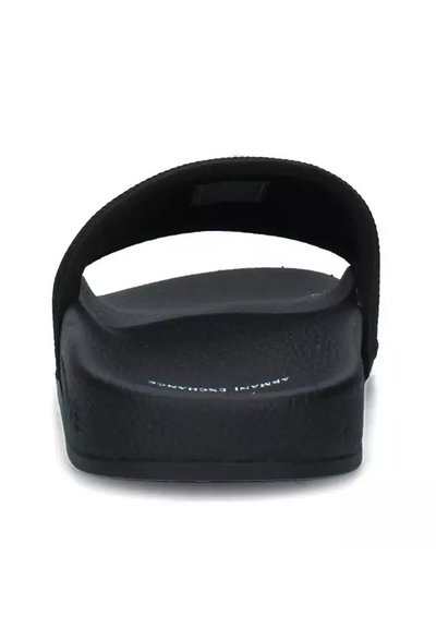 Tongs noires avec une semelle texturée et une large sangle unique. Le design est minimaliste et fabriqué à partir d'un matériau semblable au caoutchouc.
