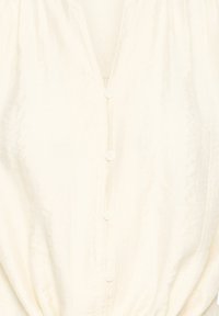 Blouse ivoire avec boutons recouverts sur le devant et texture jacquard florale subtile.