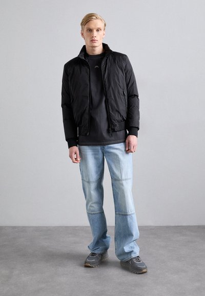Black, short puffer jacket with a stand-up collar, zippered front, and side pockets. Worn over a black t-shirt and light blue jeans. Gray sneakers.
