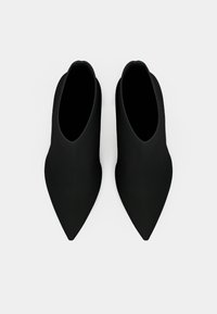 Paire de bottines noires à bout pointu avec une texture lisse vues de dessus sur un fond blanc.