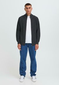 Grå ribbade zip-up cardigan med hög krage, bärs över en vit T-shirt och kombineras med blå denimjeans och vita sportskor.