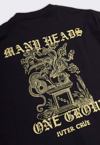 Maglietta nera con design dorato di un drago multicefalo su un piedistallo etichettato 2002, circondato dal testo "Many Heads One Grow" e "Iuter Crüe."