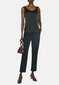 Top in satin nero con scollatura ampia abbinato a pantaloni neri su misura. Gli accessori includono una borsa bordeaux e décolleté coordinate.