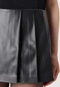 Black pleated faux leather skirt with a smooth texture and varying sheen. Features structured folds and a clean hemline.