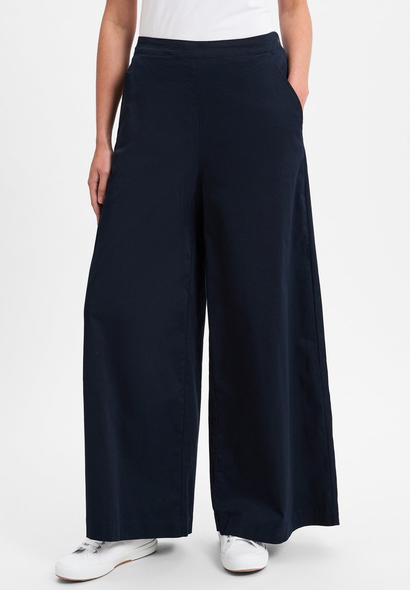 Marineblauwe wijde broek met een gladde textuur, voorzien van zijzakken en een comfortabele tailleband, gecombineerd met witte sneakers.