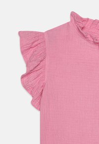 Rosa, strukturert stofftopp med volanger på korte ermer og samlet halslinning. Materialet virker mykt og lett.