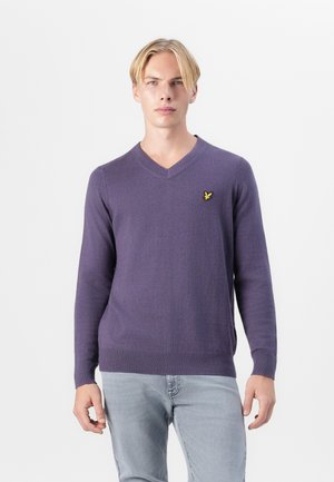 Lilla genser med V-hals laget av myk stoff, med lange ermer og en liten gul logo på brystet. Ribbet kant og mansjetter.