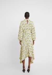 Robe fleurie avec une base blanche, ornée de motifs verts et noirs, manches longues bouffantes, dos ajouré et ourlet asymétrique.