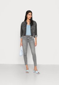 Casaco de ganga cinza escuro, blusa azul clara com um padrão decorativo, jeans skinny cinza, mala azul clara e sandálias de salto bloco de ponta aberta.