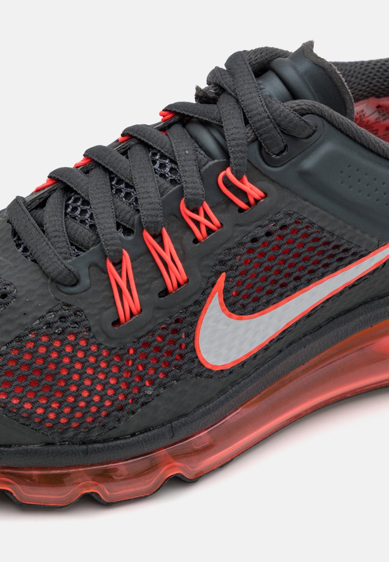 Zapato deportivo negro con acentos rojos, parte superior de malla y suela acolchada. Presenta un prominente logo de swoosh de Nike en plata.