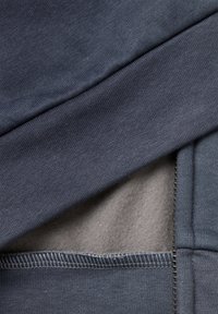 Tejido azul oscuro con una textura suave, con una capa de forro polar gris debajo. Costuras visibles y un detalle de bolsillo.