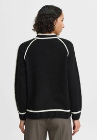 Pullover nero con accenti bianchi col colletto e l'orlo. Texture morbida e pelosa, con una vestibilità comoda. Maniche raglan. Design semplice e moderno.