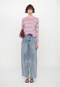 Pink and gray striped knit sweater, high-waisted light wash wide-leg jeans, black strappy sandals, holding a small burgundy handbag.