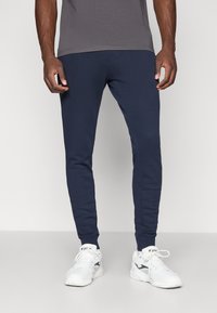 Mørkeblå treningsbukser med smal passform, laget av mykt stoff, med elastisk midje og ribbede mansjetter ved anklene.