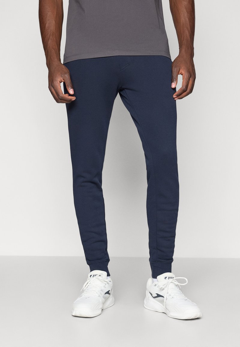 Mørkeblå treningsbukser med smal passform, laget av mykt stoff, med elastisk midje og ribbede mansjetter ved anklene.