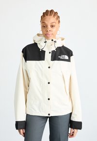 Cream and black waterproof jacket with a hood, featuring a full zip closure and front pockets, made of textured fabric, logo on chest.